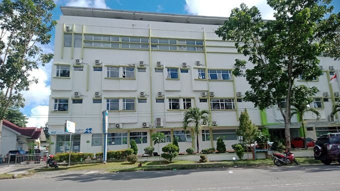 Aerial view of a hospital building with mountains and clouds in the background under a partly cloudy sky